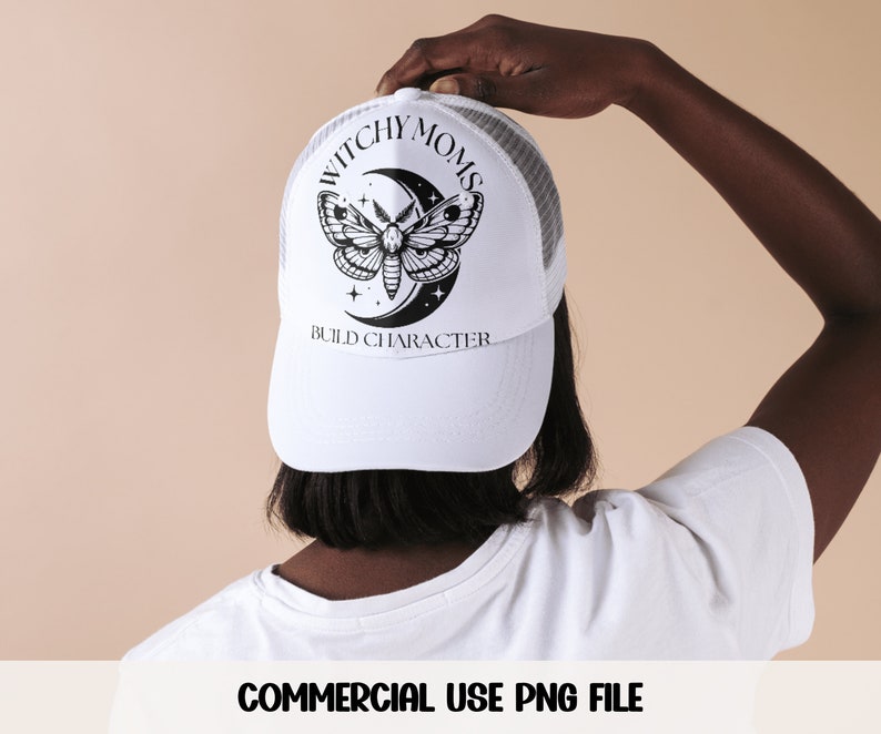 K&ouml;nnte beinhalten: Wei&szlig;e Trucker-Kappe mit einem schwarz-wei&szlig;en Motiv aus einem Nachtfalter und einem Halbmond. Der Text "Witchy Moms Build Character" ist auf der Vorderseite der Kappe aufgedruckt.