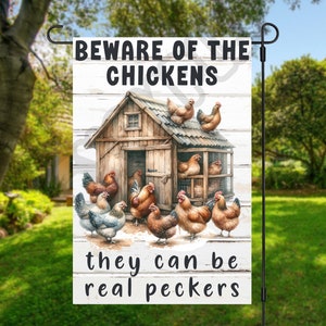 Puede incluir: Una bandera de jardín blanca con un gallinero de madera marrón y gallinas. El texto en la bandera dice "Cuidado con las gallinas, pueden ser verdaderas picadoras".