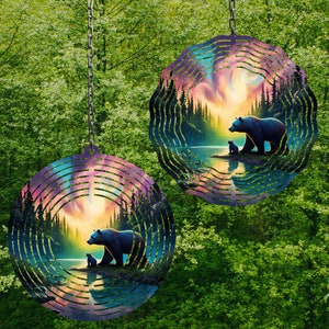 Peut inclure: Deux mobiles à vent métalliques de forme circulaire. Les mobiles représentent une ourse et son ourson debout au bord d'un lac dans un décor de forêt. L'arrière-plan est un coucher de soleil coloré avec un ciel bleu, rose et violet.