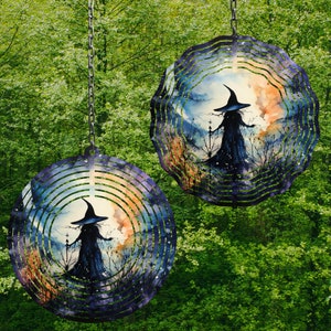 May include: Two metal wind spinners with a circular design. Each spinner features a watercolor-style image of a witch in a forest setting. The spinners are painted in shades of purple, blue, and orange.