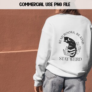 May include: White sweatshirt with a black graphic design featuring a cat reading a book with crystals and the text "Read Books, Be Kind, Stay Weird".
