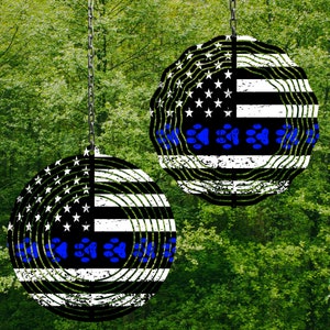 May include: Two round metal hanging decorations with a distressed American flag design. The black and white flag features blue paw prints and a blue line. The decorations hang from a chain against a green background.