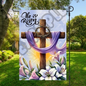 May include: A garden flag with a wooden cross draped in purple fabric and surrounded by white lilies. The text "He is Risen" is printed in white on a blue background.
