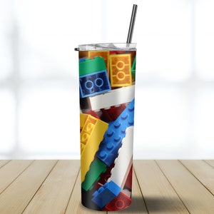 May include: A stainless steel tumbler with a colorful design of plastic building blocks. The tumbler has a clear lid and a black straw.