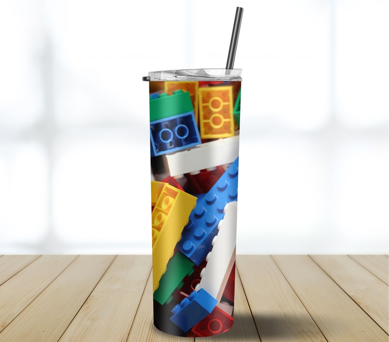 May include: A stainless steel tumbler with a colorful design of plastic building blocks. The tumbler has a clear lid and a black straw.
