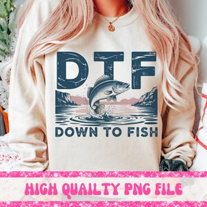 May include: Beige sweatshirt with a graphic that says "DTF" above a leaping fish illustration. Below the fish, the text reads "DOWN TO FISH". The design includes a lake scene with mountains and water ripples. The bottom of the image has the text "HIGH QUAILTY PNG FILE".