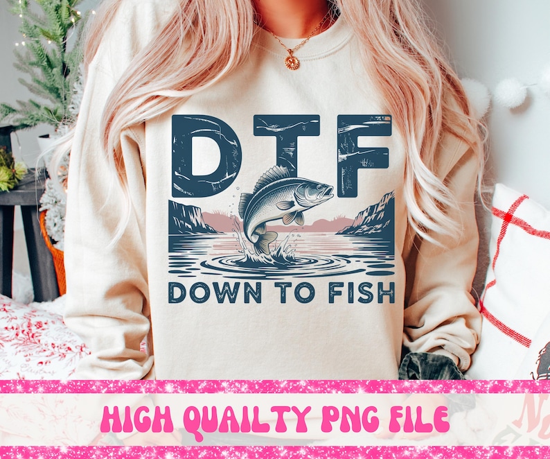 May include: Beige sweatshirt with a graphic that says "DTF" above a leaping fish illustration. Below the fish, the text reads "DOWN TO FISH". The design includes a lake scene with mountains and water ripples. The bottom of the image has the text "HIGH QUAILTY PNG FILE".