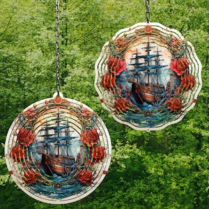 May include: Two metal wind spinners with a nautical theme. Each spinner features a detailed illustration of a sailing ship with red, white, and blue accents. The spinners are suspended from a chain and have a circular design with a swirling pattern.