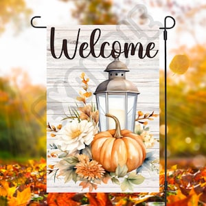 Puede incluir: Una bandera de jardín de bienvenida con un fondo de madera blanqueada con una linterna, una calabaza y follaje de otoño. La linterna es gris con una vela blanca en su interior. La calabaza es naranja con hojas verdes. El follaje es una mezcla de verde, marrón y naranja.