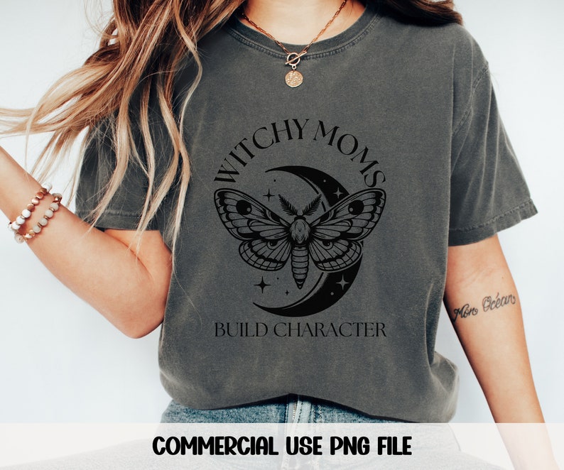 K&ouml;nnte beinhalten: Ein dunkelgraues T-Shirt mit einem schwarzen Grafikdesign, das eine Sichelmond, einen Nachtfalter und Sterne zeigt. Der Text "Witchy Moms Build Character" ist auf das Shirt gedruckt.
