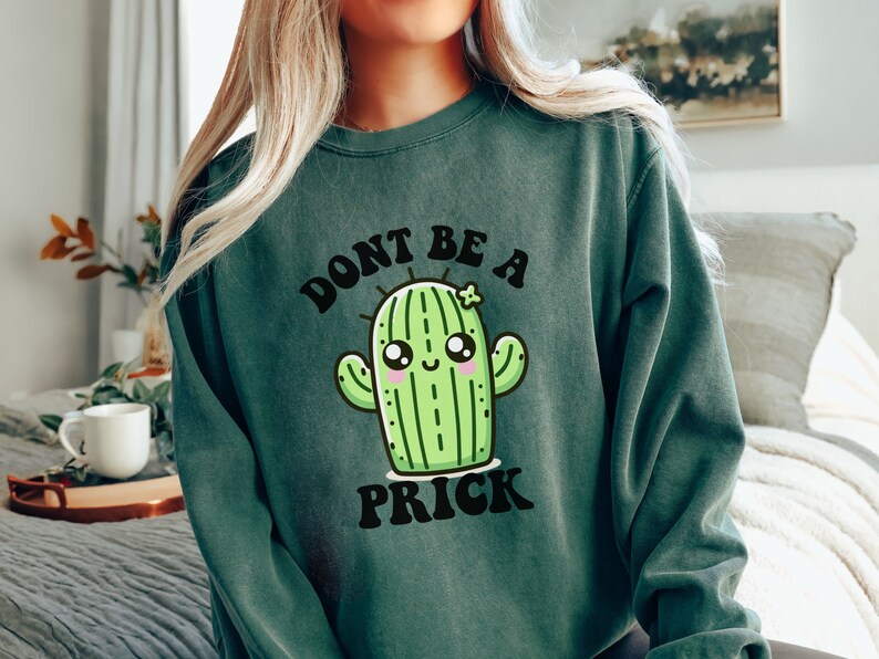 May include: Green sweatshirt with a cartoon cactus and the text "Don't be a prick" in black.