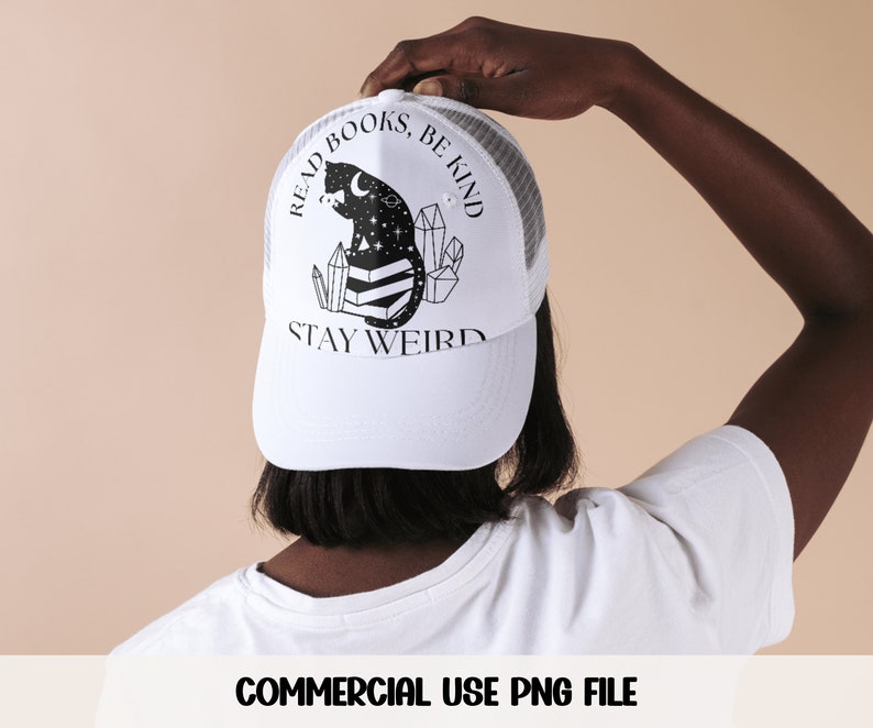 May include: White trucker hat with a black and white illustration of a cat sitting on books with crystals and stars. The text "Read Books, Be Kind, Stay Weird" is printed on the hat.