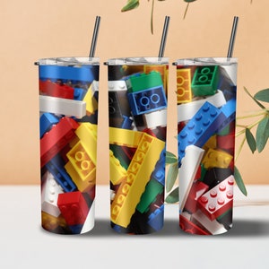 May include: Three stainless steel tumblers with lids and straws. Each tumbler features a different design of colorful plastic building blocks.