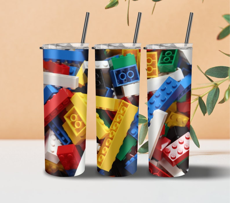 May include: Three stainless steel tumblers with lids and straws. Each tumbler features a different design of colorful plastic building blocks.