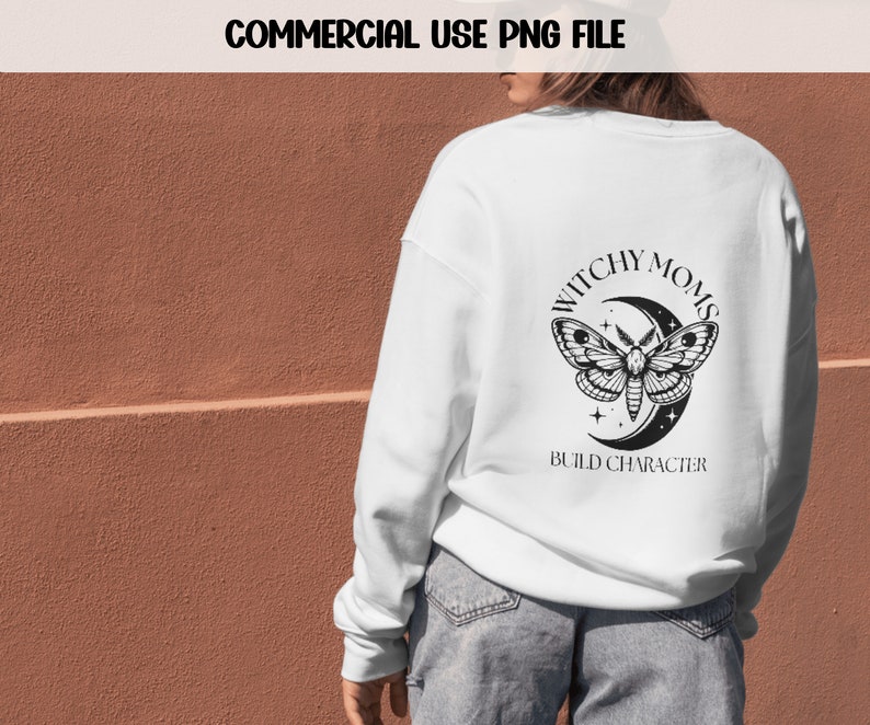 K&ouml;nnte beinhalten: Wei&szlig;er Pullover mit einem schwarz-wei&szlig;en Motiv eines Nachtfalters und eines Halbmondes. Der Schriftzug lautet "Witchy Moms Build Character".