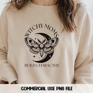 K&ouml;nnte beinhalten: Ein beiger Pullover mit dem Text "Witchy Moms Build Character" in schwarzen Buchstaben. Ein schwarzer Halbmond mit einem Nachtfalter ist mittig auf dem Pullover platziert.