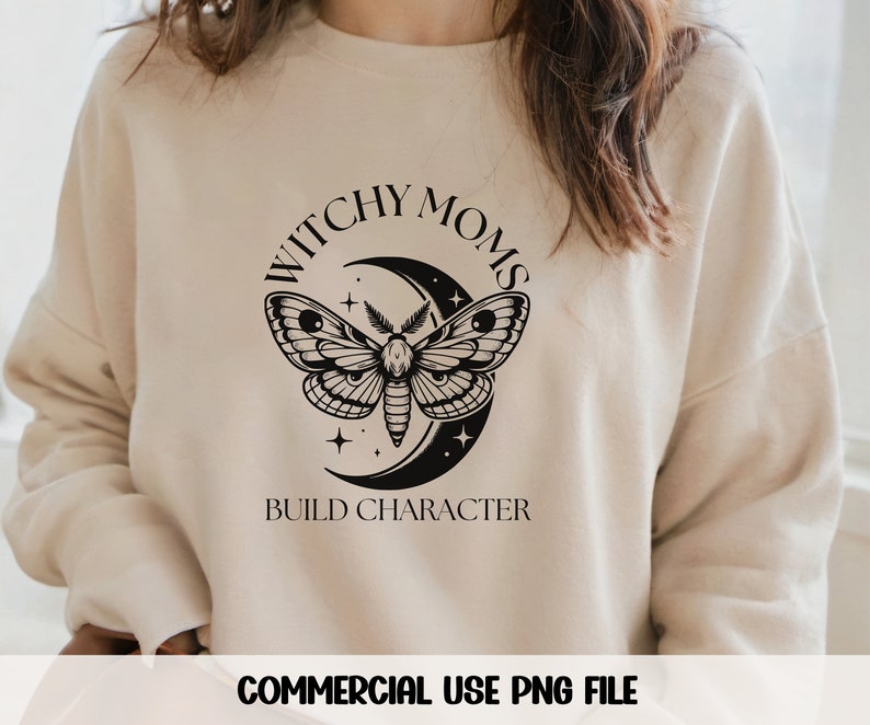 K&ouml;nnte beinhalten: Ein beiger Pullover mit dem Text "Witchy Moms Build Character" in schwarzen Buchstaben. Ein schwarzer Halbmond mit einem Nachtfalter ist mittig auf dem Pullover platziert.