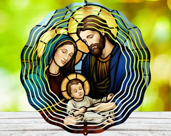 May include: A metal wind spinner with a stained glass design of the Holy Family. Mary, Joseph, and baby Jesus are depicted in a blue, gold, and red color scheme. The spinner has a circular shape with multiple layers of metal.