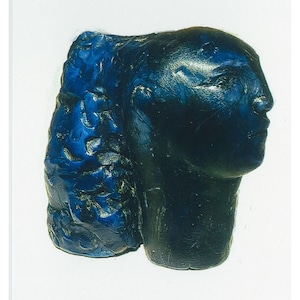 May include: A blue ceramic sculpture of a person's head and shoulders. The sculpture is in profile, with the person's face turned to the right. The sculpture is made of a rough, textured material.