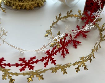 May include: A gold, white, and red snowflake garland with a repeating pattern of snowflakes. The garland is made of paper and is perfect for decorating for the holidays.
