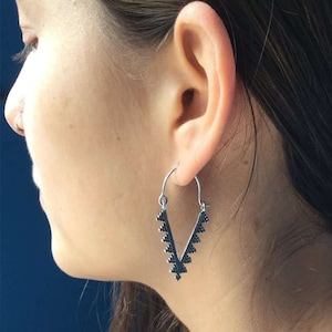 May include: Silver hoop earrings with a V-shaped design. The earrings are decorated with small, black triangles.