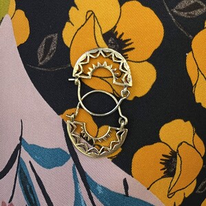 May include: A pair of gold hoop earrings with a sunburst design. The earrings are hanging on a floral fabric background.