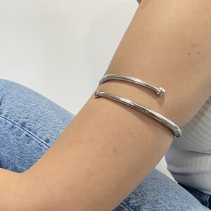 May include: A silver arm cuff with a rounded end. The cuff is worn on the upper arm.
