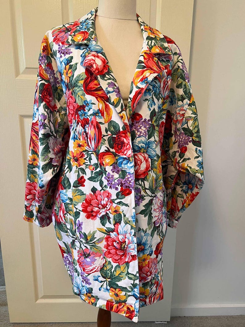 May include: A floral print blazer featuring a vibrant mix of red, pink, blue, yellow, and purple flowers on a white background. The blazer has a classic collar and long sleeves, offering a colorful and eye-catching design.