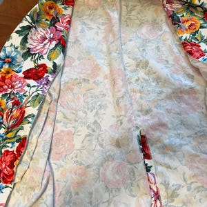 May include: A white floral print blazer featuring a vibrant array of red, pink, yellow, and blue flowers. The open blazer showcases a soft, lightweight fabric with a colorful botanical design, perfect for adding a touch of spring to any outfit.