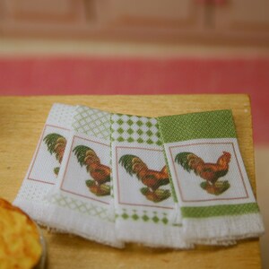 Pode incluir: Conjunto de quatro toalhas de cozinha com padrão xadrez verde e branco. Cada toalha apresenta uma ilustração de um galo com crista vermelha e fundo verde.