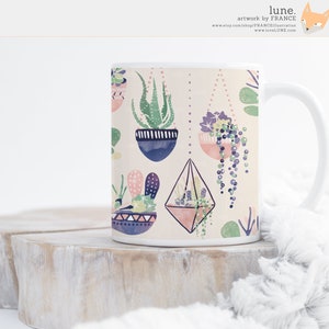 May include: White ceramic mug with a colorful pattern of hanging succulents and cacti. The pattern includes geometric shapes, pink, blue, and green colors.