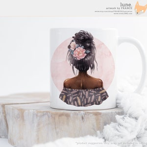 Puede incluir: Taza de cer&aacute;mica blanca con un gr&aacute;fico de una mujer con cabello negro largo, usando una corona de flores y una blusa de hombros descubiertos con estampado. El fondo es un c&iacute;rculo rosa.