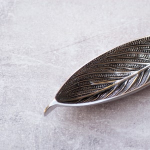 May include: A silver leaf-shaped dish with a textured surface. The dish is made of metal and has a delicate design.