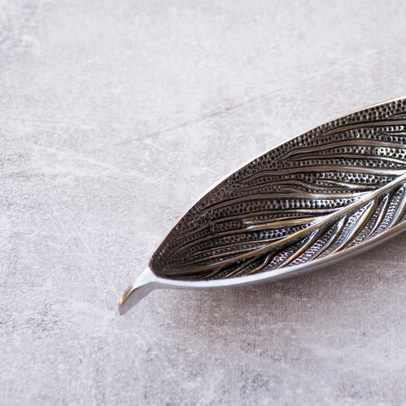 May include: A silver leaf-shaped dish with a textured surface. The dish is made of metal and has a delicate design.