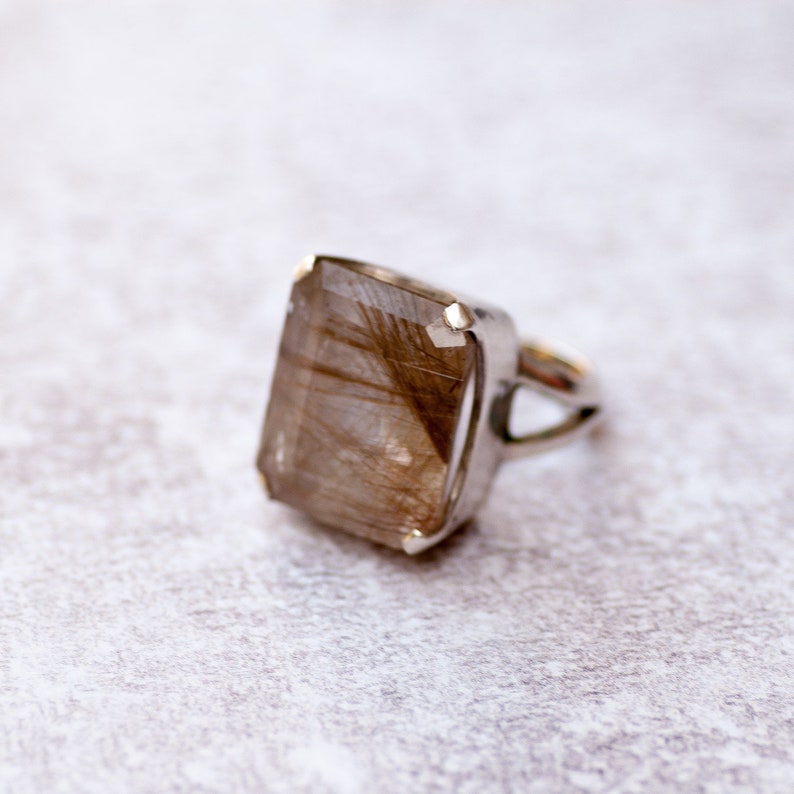 May include: A silver ring with a large, rectangular, clear quartz stone with brown inclusions. The stone is set in a bezel setting.
