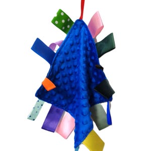 May include: A blue, textured baby tag blanket with colorful satin ribbons attached. The blanket has a yellow ring and red ribbon for hanging. Ribbons are various colors, including green with white polka dots, pink, and blue.