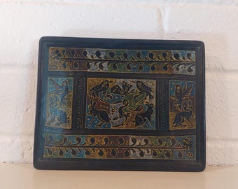 Puede incluir: Bandeja decorativa rectangular azul oscuro con un diseño tallado. La bandeja presenta un panel central con pájaros, conejos y otras criaturas. El borde tiene un patrón floral repetido en tonos azules, verdes y dorados.