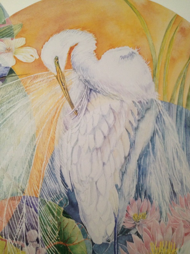 May include: Watercolor painting of a white egret preening its feathers. The bird is set against a backdrop of an orange sun, with green foliage and pink lotus flowers in the foreground. The artwork has a soft, ethereal quality.