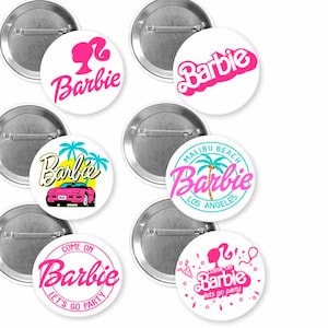 May include: A collection of white pinback buttons featuring the word "Barbie" in various pink fonts and designs. Some buttons include additional graphics like a silhouette, car, palm trees, and the phrases "Malibu Beach Los Angeles" and "Come on Barbie let's go party."