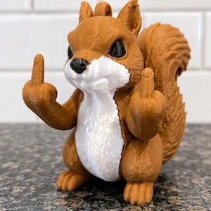 May include: A 3D printed squirrel figurine in brown and white plastic. The squirrel has a textured surface, black eyes, and a black nose. It is posed in a standing position with both arms raised, extending its middle fingers in a gesture.