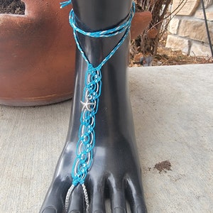 May include: A blue and white foot jewelry with a silver starfish charm. The jewelry is made of string and is tied around the foot.