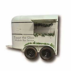 Peut inclure: Une remorque de cheval blanche transformée en service de bar mobile. Le côté de la remorque porte une inscription "Toast the Glass Mobile Bar Service".