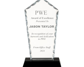 Puede incluir: Un premio de cristal transparente con una base negra. El premio tiene forma de casa puntiaguda y tiene el texto "PWE Award of Excellence Presented To JASON TAYLOR In recognition of your hard work and dedication to PWE From Office Staff 2024".