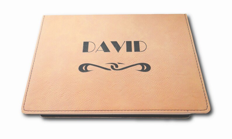 以下が含まれることがあります： 名前が「DAVID」と刻印された、薄い茶色の革製のジャーナル。ジャーナルには、名前の下に装飾的なデザインが施されています。