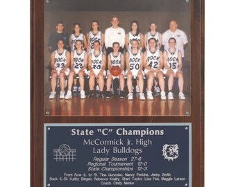 May include: A framed team photo of the McCormick Jr. High Lady Bulldogs basketball team, celebrating their State "C" Championship. The photo is set on a dark wood plaque with a blue plate below, listing team details and player names.