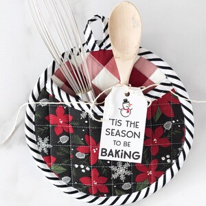 May include: A black and white striped pot holder with a red and green floral print. The pot holder has a pocket for utensils and a tag that says "'Tis the season to be baking" with a snowman illustration.