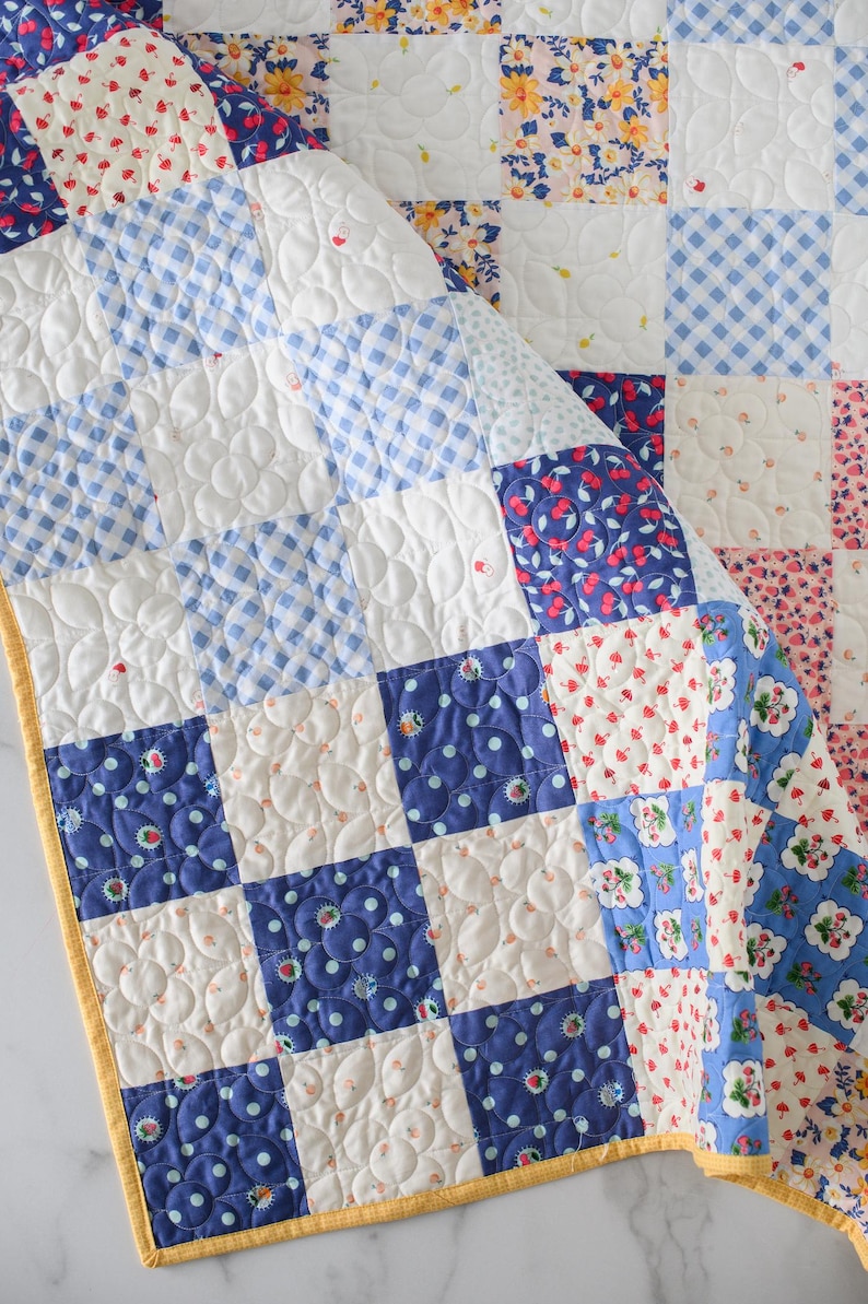 May include: A patchwork quilt with a variety of patterned squares in white, blue, and floral prints. The quilt features a yellow border and is quilted with a floral pattern. The quilt is made of cotton and is approximately 60 inches by 60 inches.