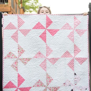 May include: A pink and white quilt with a pinwheel pattern. The quilt is made with different pink fabrics with white polka dots, floral patterns, and solid pink.
