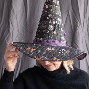 May include: A black witch hat with a patchwork design and a purple ribbon. The hat is quilted and has a pointed crown. The hat is being worn by a person with blonde hair.