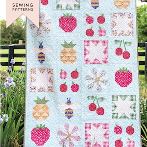 Könnte beinhalten: Eine blaue und weiße Quiltdecke mit Sommerthema. Die Quiltdecke zeigt verschiedene Motive, darunter Ananas, Erdbeeren, Kirschen, Bienen und Blumen. Die Quiltdecke trägt den Titel "Summer Sugar Quilt".